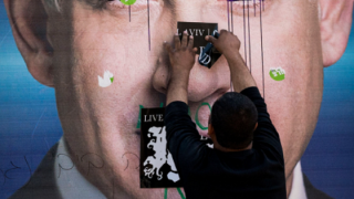 A man puts a sticker on a vandalized campaign poster of PM Benjamin Netanyahu. Photo: Danielle Shitrit/Flash90